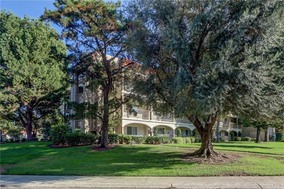 Front view of a multi-story apartment building with balconies surrounded by trees and greenery.
