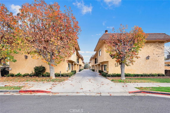 Front view of a residential building with multiple units and autumn trees lining the entrance.