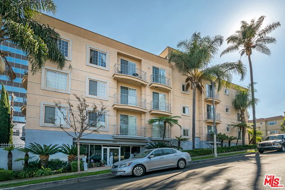 Front view of a four-story residential building with balconies and palm trees.