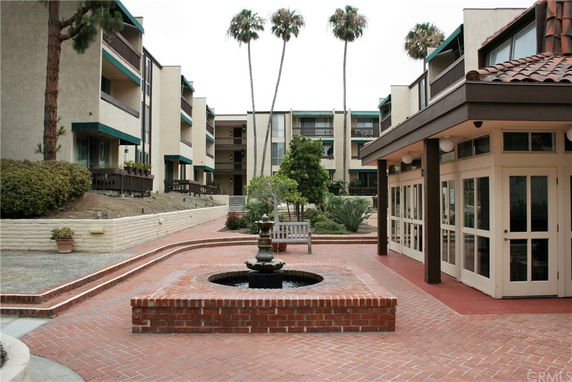 View of a residential building complex with a brick pathway and a small fountain in the courtyard.