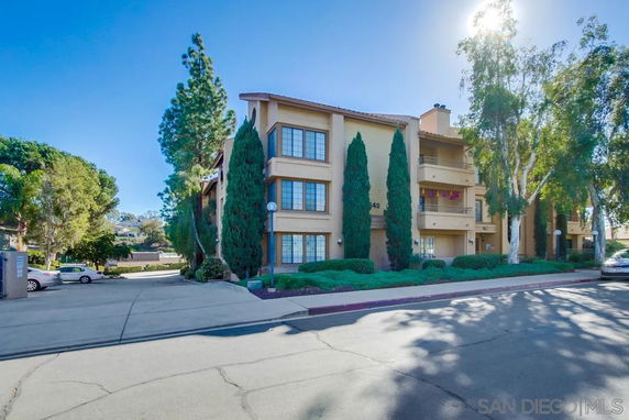 Front view of a multi-story apartment building with balconies and tall trees.