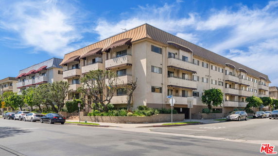 Front view of a multi-story apartment building with balconies and a sloped roof.