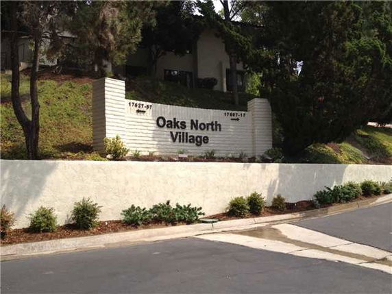 Front view of the entrance to a community named Oaks North Village with a sign on a white wall.