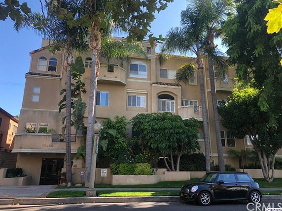 Front view of a multi-story apartment building with balconies and palm trees.