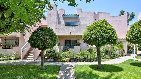Front view of a multi-story residential building with a flat roof and decorative trees.