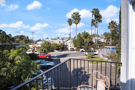View of surrounding residential area from a balcony with palm trees and parked cars.