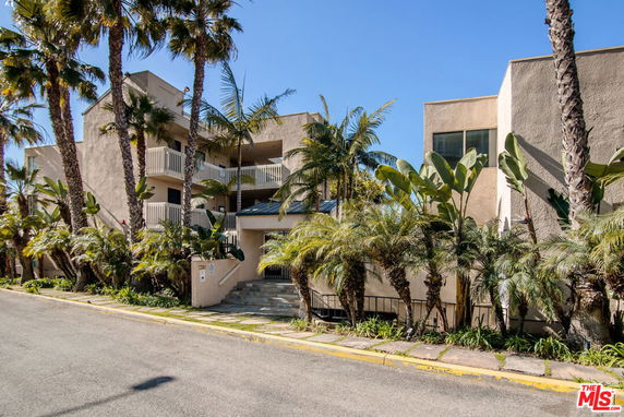 Front view of a multi-story apartment building with balconies and tropical plants.