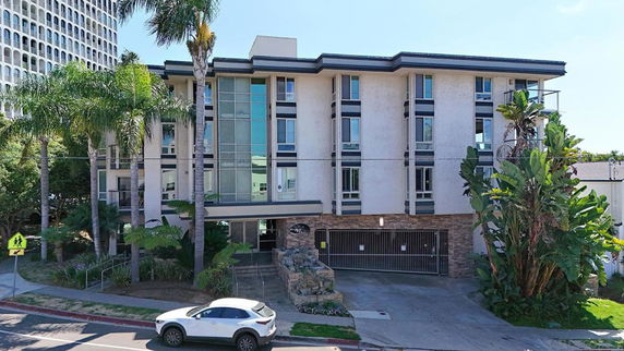 Front view of a multi-story building with a gated parking entrance and large windows.