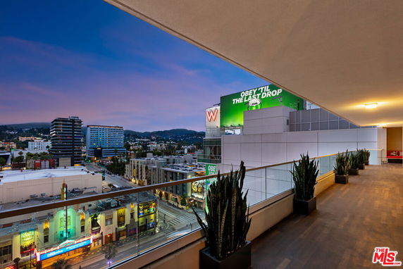 Panoramic city view from a building balcony at dusk with illuminated billboards and buildings.