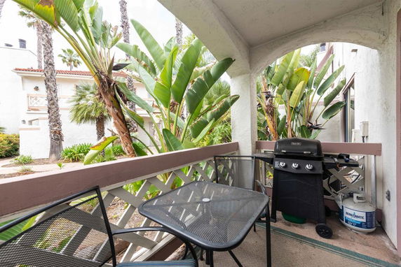 View from a balcony with outdoor furniture and a grill, overlooking tropical plants and a nearby building.