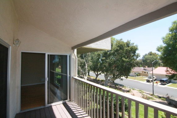 View from a balcony overlooking a residential street with trees and houses.