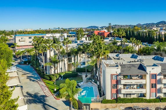 Aerial view of a residential complex with several multi-story buildings, surrounded by palm trees and other greenery.