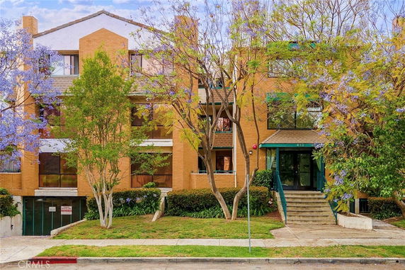 Front view of a multi-story brick building with trees and plants.