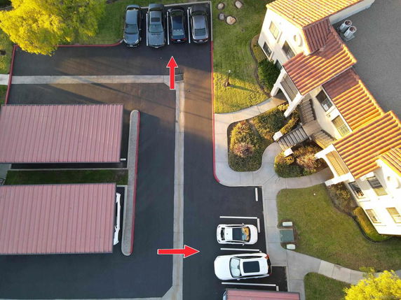 Aerial view of an outdoor parking area with several cars and covered parking spaces next to a building.