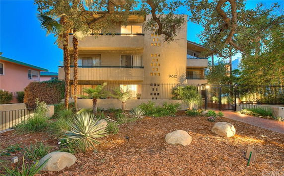 Front view of a multi-story residential building with balcony and surrounding trees.
