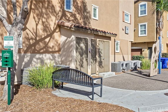 Front view of a multi-story building with a bench and air conditioning units.