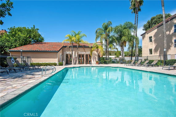 Outdoor swimming pool area with lounge chairs and nearby building.