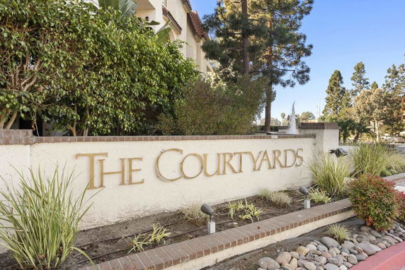 Front view of a building complex sign labeled 'The Courtyards' with greenery and a fountain.