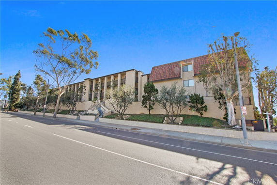 Front view of a multi-story building with a stairway entrance and surrounding trees.