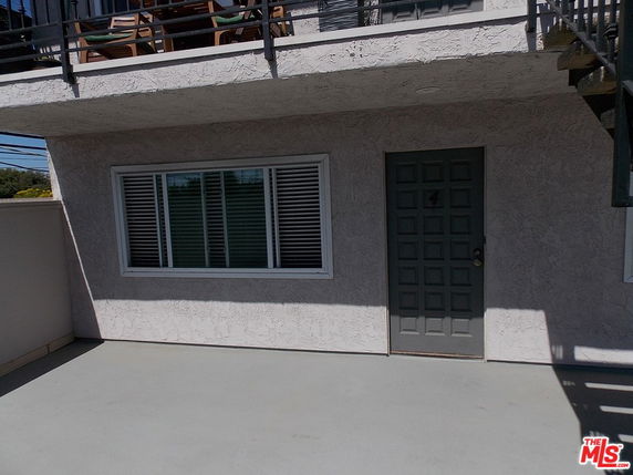 Front view of a building with a single door and window, upper balcony visible.