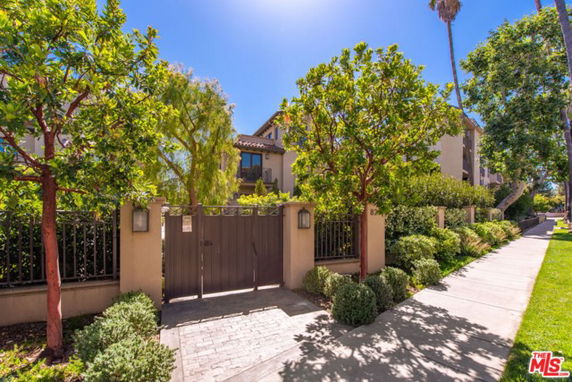 Front view of a residential building with a gated entrance and surrounding trees.