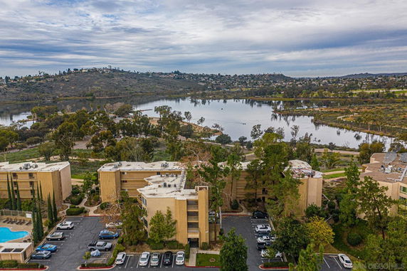 Aerial view of multiple apartment buildings near a body of water with surrounding greenery and hills.