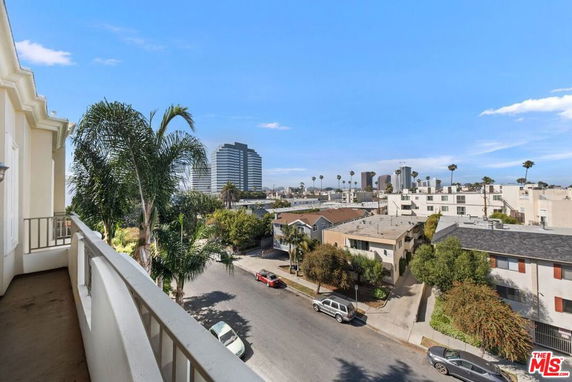 View of a cityscape with buildings and palm trees from a balcony.