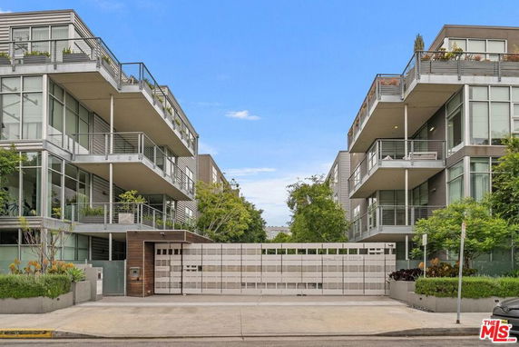 Front view of a modern multi-story residential building with glass balconies and a gated entrance.