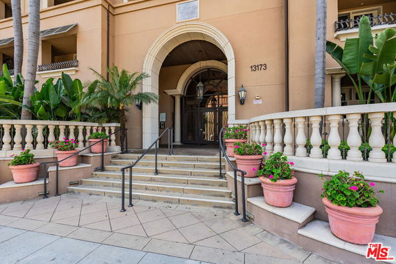 Front view of a building entrance with an arched doorway and stairway adorned with potted plants.