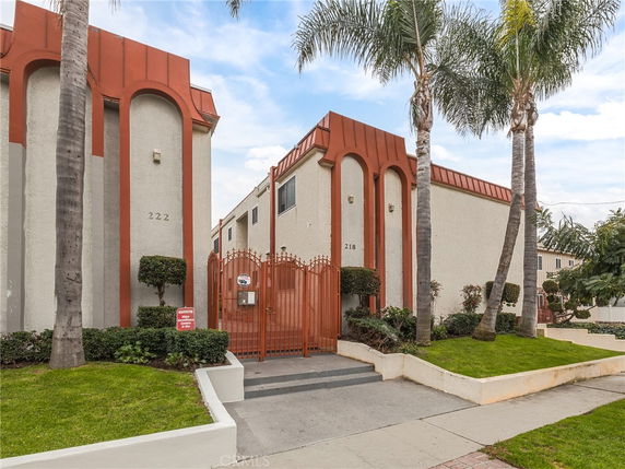 Front view of a two-story building with gated entrance and palm trees.