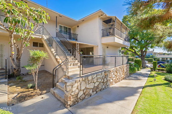 Front view of a two-story house with an external staircase and stone wall.