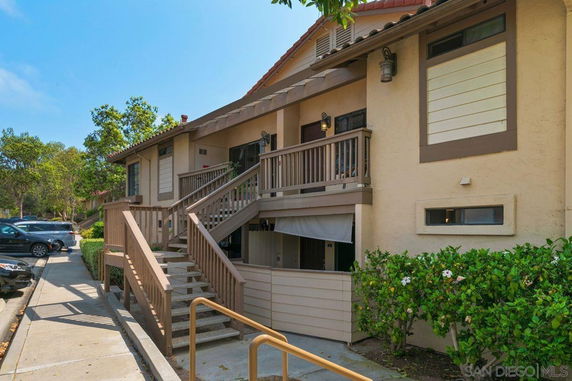 Front view of a multi-level beige house with a wooden staircase and railing leading to the entrance.