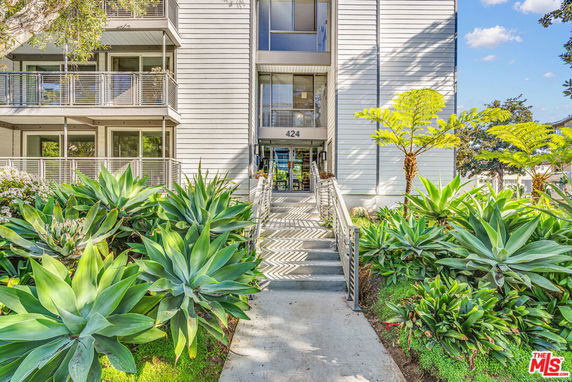 Front view of a multi-story building with balconies and lush greenery.