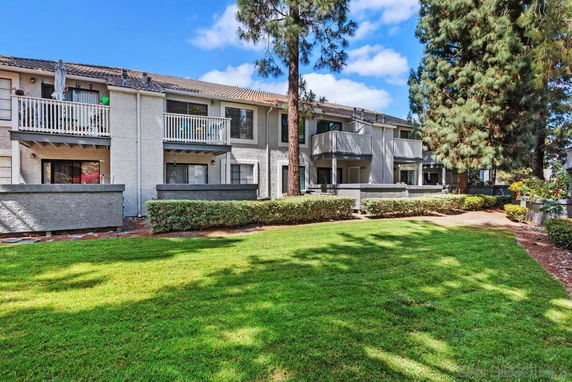 Front view of a two-story residential building with balconies and surrounding trees.