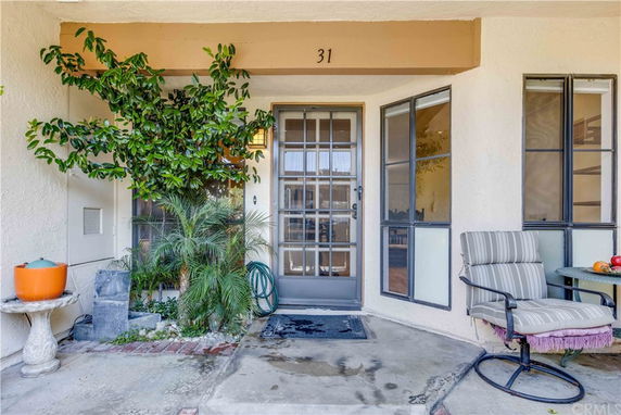 Front view of a house with a glass door entry and adjacent windows, featuring outdoor sitting area and potted plants.