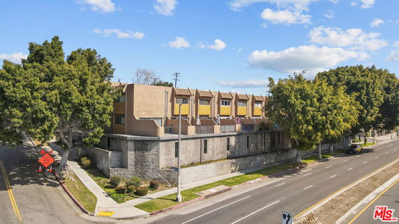 Front view of a multi-story building with a stone retaining wall and trees along the street.