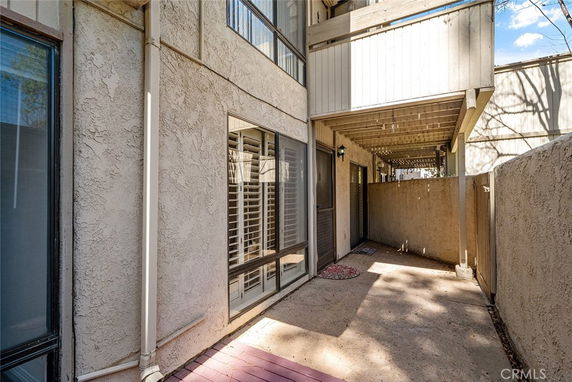 Exterior view of a house with beige stucco walls, a fenced patio area, and an overhead balcony.
