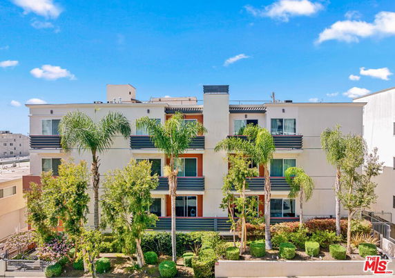 Front view of a multi-story building with balconies and palm trees.