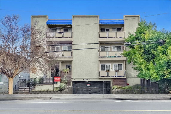 Front view of a multi-story apartment building with balconies and a gated entrance.