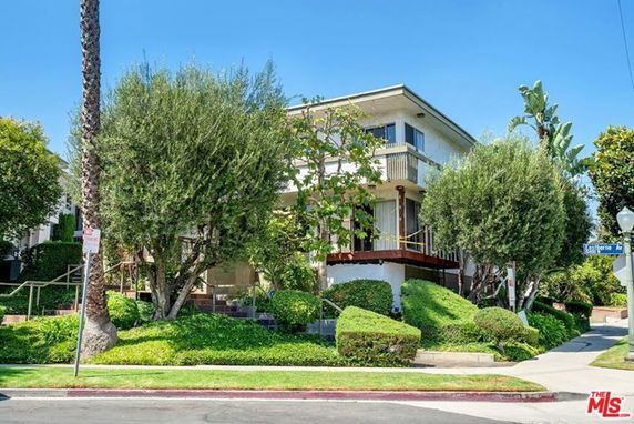 Front view of a two-story house with a balcony surrounded by trees and shrubs.