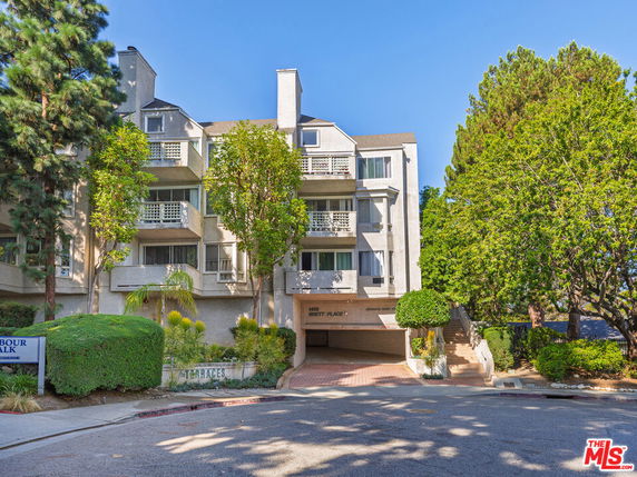 Front view of a multi-story apartment building with balconies and lush greenery.