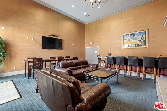 Room with brown leather couches, a bar area with stools, and a wall-mounted TV.