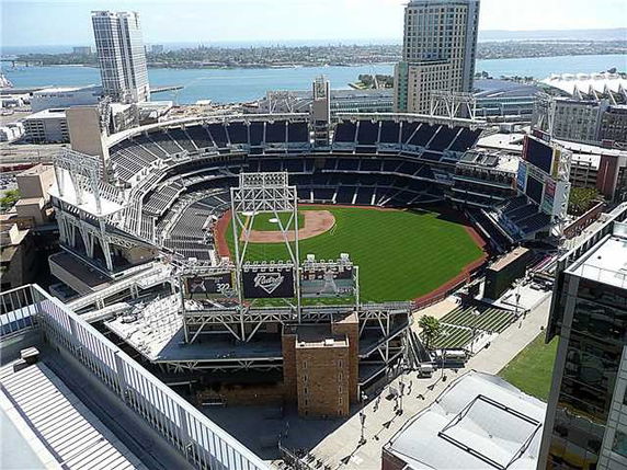 Aerial view of a baseball stadium with surrounding buildings and water in the background.