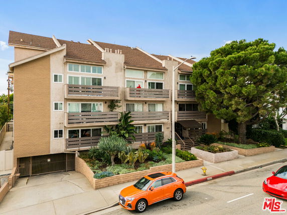 Front view of a multi-story residential building with balconies and a sloped roof.