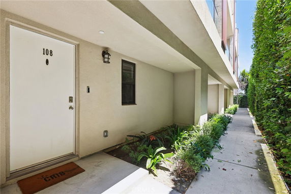 Front view of an apartment entrance with door number 108, featuring a walkway and greenery.