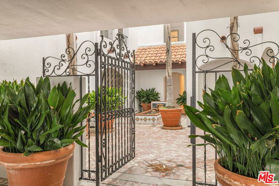 Front view of a Mediterranean-style building with a wrought iron gate, terracotta roof tiles, and potted plants.
