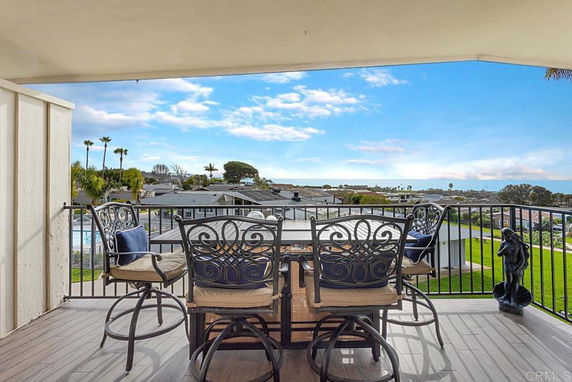 View from a balcony with outdoor furniture overlooking rooftops and a distant ocean.