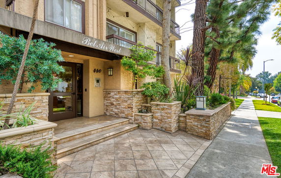 Front view of a multi-story building with greenery and tiled entrance.