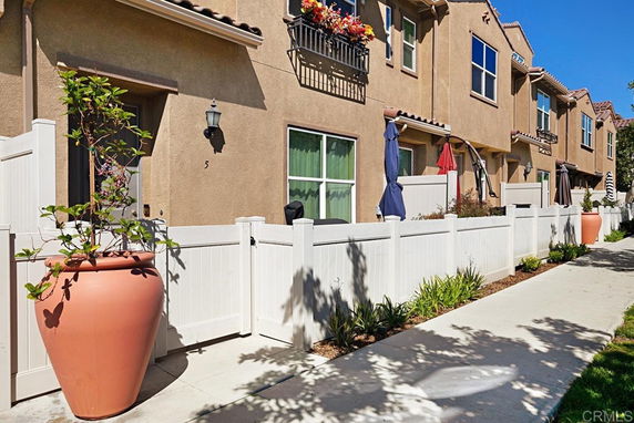 Front view of a two-story townhouse with white picket fence and potted plants.