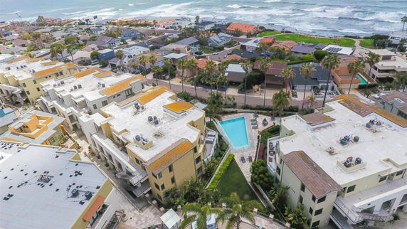 Panoramic view of residential buildings with a swimming pool and ocean in the background.